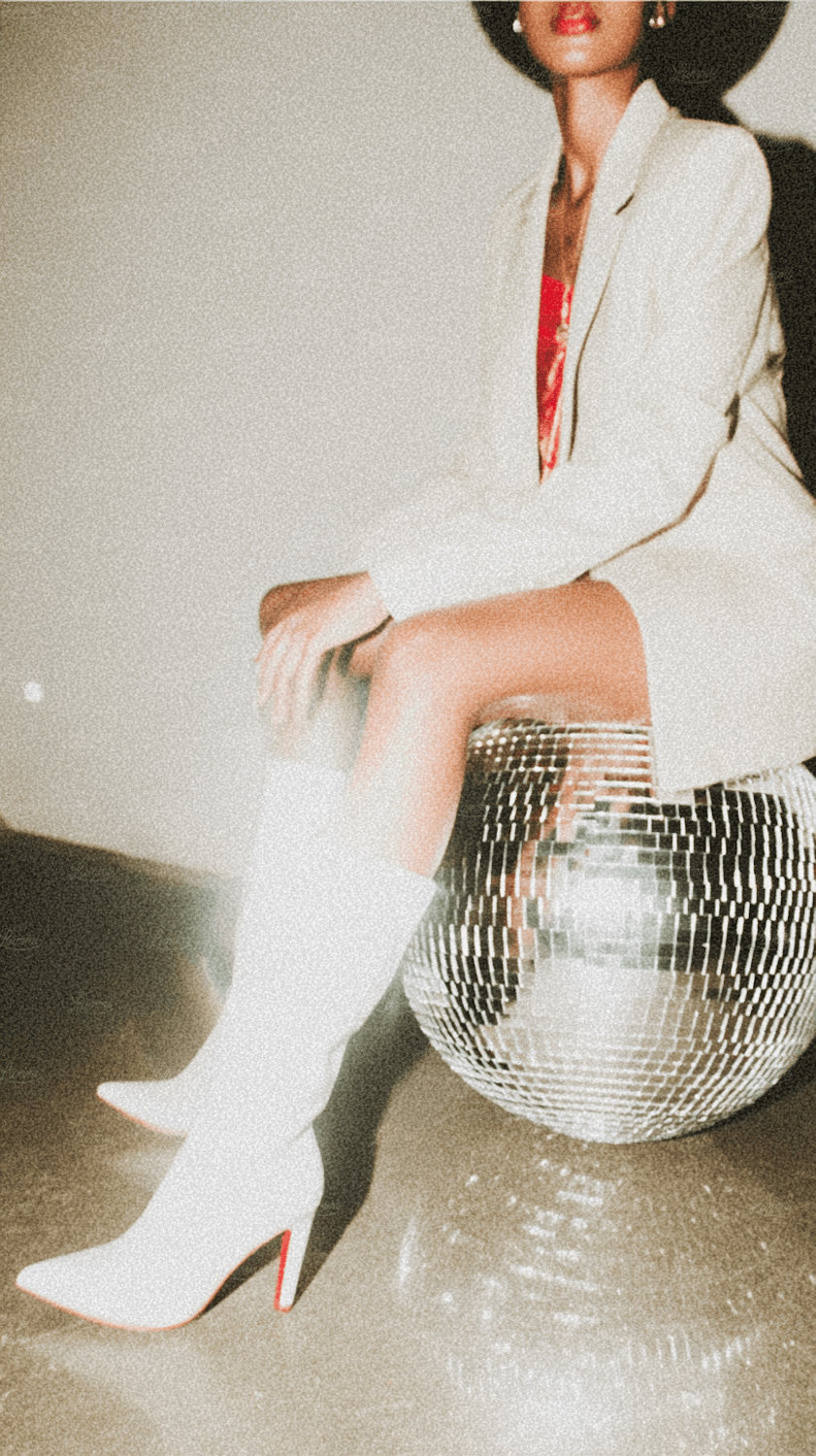 Une femme en blazer blanc et bottes blanches assise sur une boule à facettes